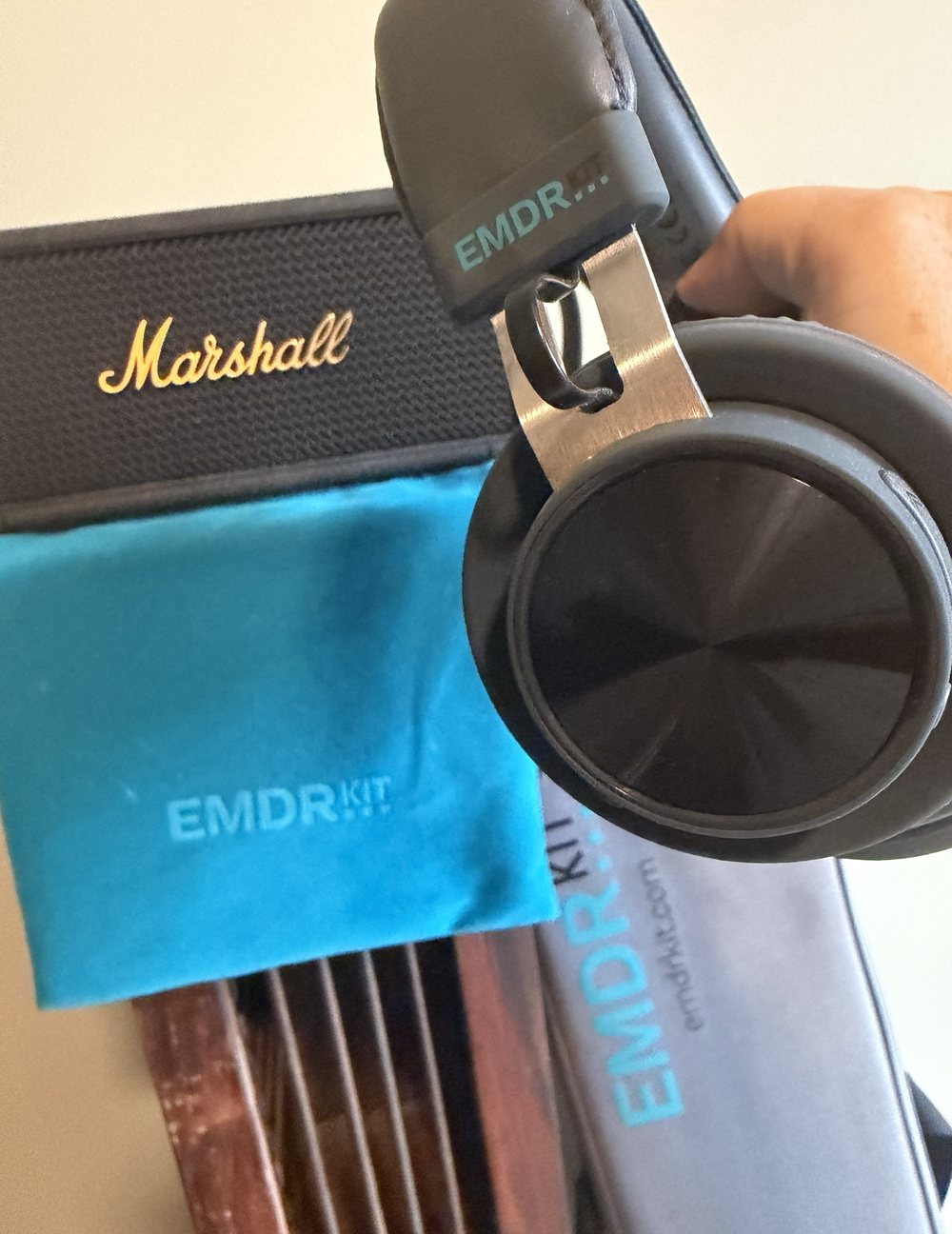 Casque EMDR tenu à la main devant une enceinte Marshall et la pochette du matériel