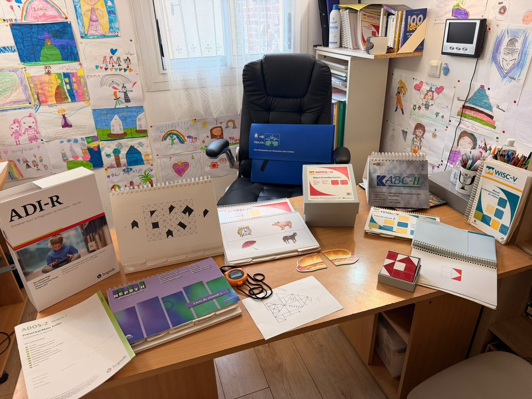 Le bureau du cabinet, avec le matériel de passation des tests et des dessins d'enfants au mur